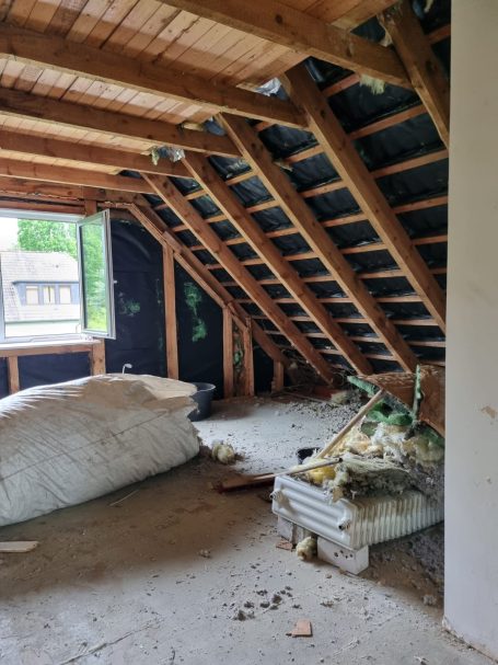 Dachboden mit Holzrahmen, isoliertem Bereich und Baustellenmaterialien.