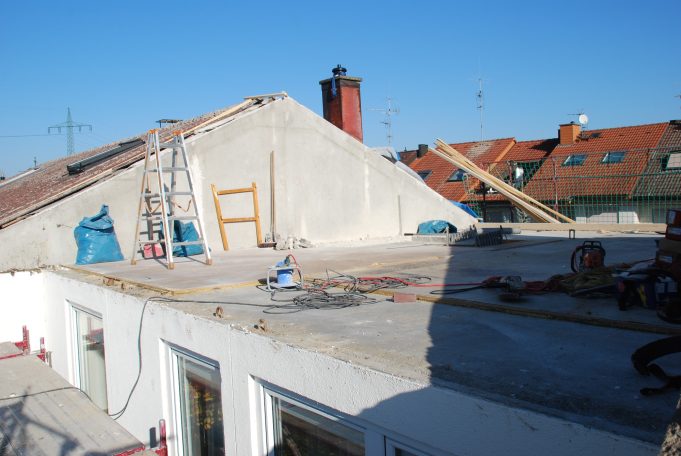 Blick auf ein Bauprojekt mit Dacharbeiten, Gerüsten und Baustellenmaterial.