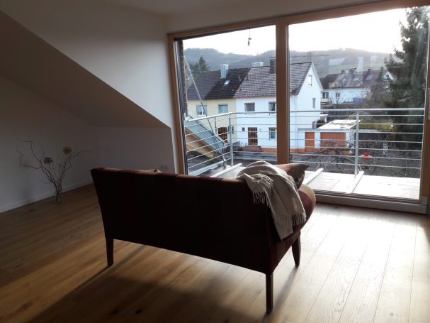 Wohnzimmer mit einem Sofa und Blick auf eine belebte Straße und Bäume.